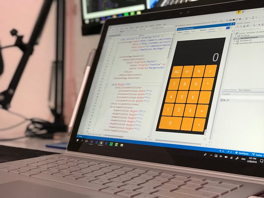 A close-up view of a laptop computer with a white keyboard and slim profile, displaying a software development environment with lines of code in different colors on the left side of the screen. The ri